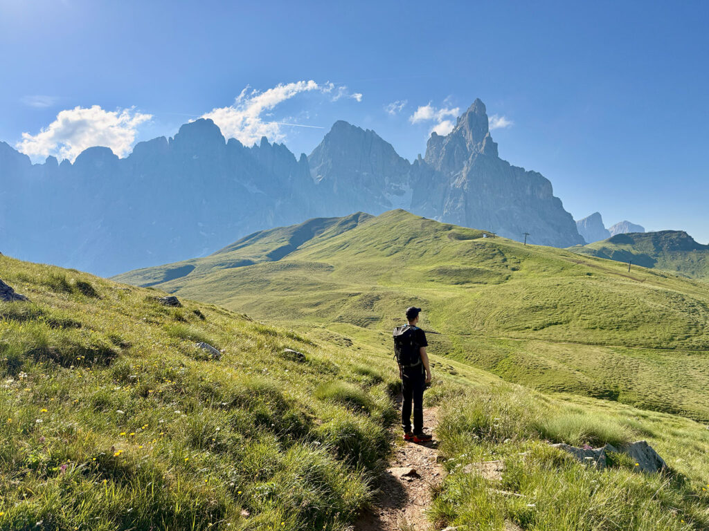 Wanderer auf einem Pfad durch grüne Bergwiesen vor den Pale di San Martino.