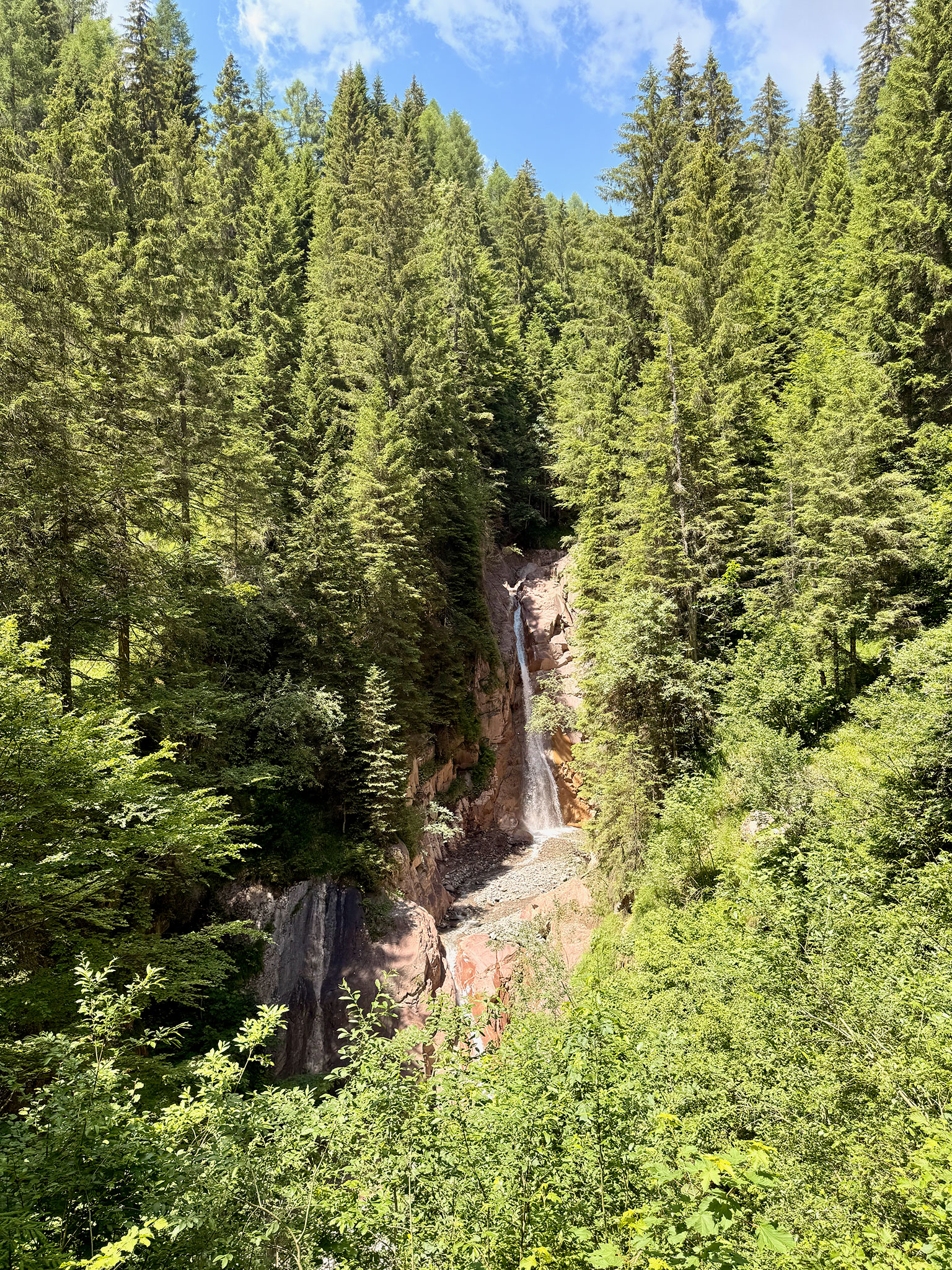 Die Cascata di Barezze stürzt durch eine schmale Felsschlucht, umgeben von dichtem grünem Wald.