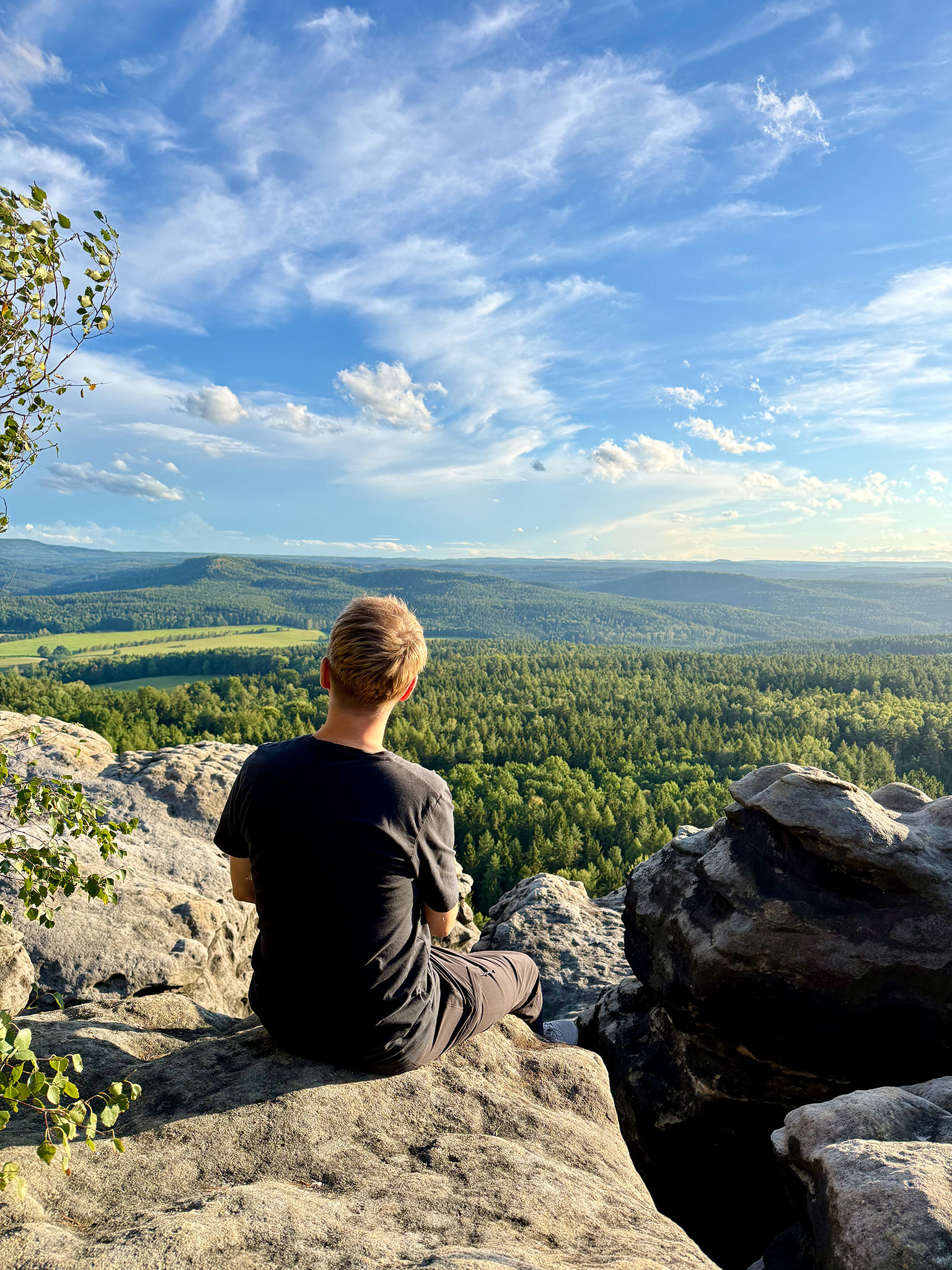 Wanderer auf einem Felsen des Gohrischsteins mit Aussicht über die bewaldete Sächsische Schweiz