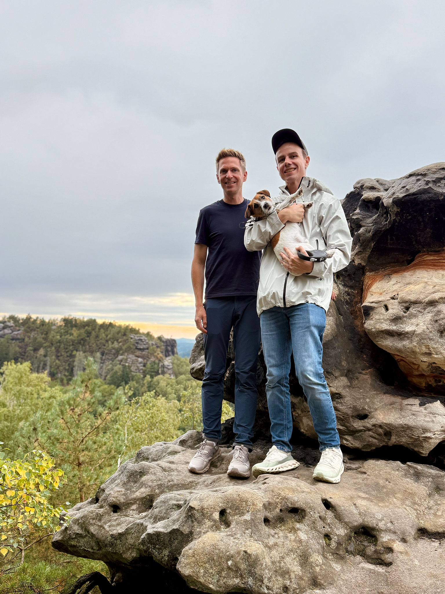 Zwei Wanderer mit Hund auf dem Papststein mit Blick über die Felsen und Wälder der Sächsischen Schweiz