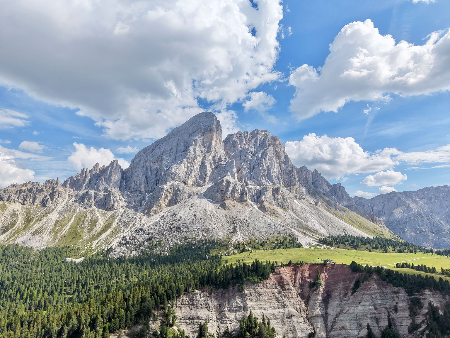 Blick auf den Peitlerkofel mit grünen Almwiesen und Wald am Passo delle Erbe.