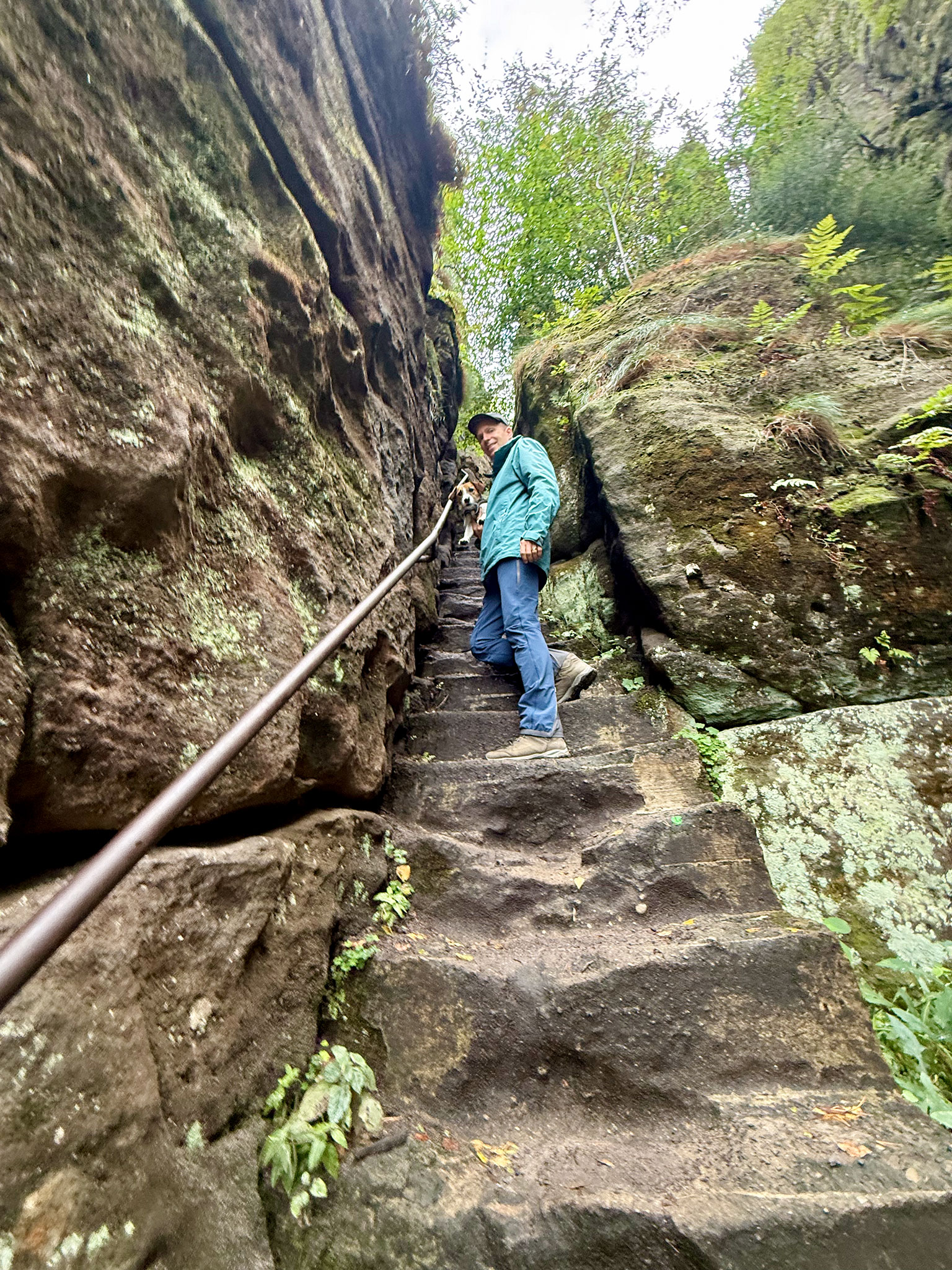 Wanderer mit Hund auf einer engen Steintreppe zwischen den Felsen am Pfaffenstein.